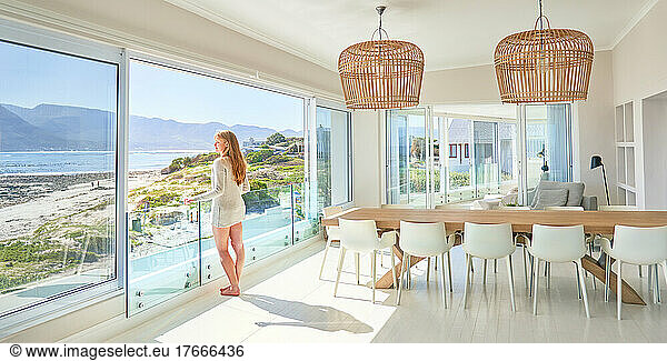 Young woman standing at sunny,  luxury patio door with ocean view