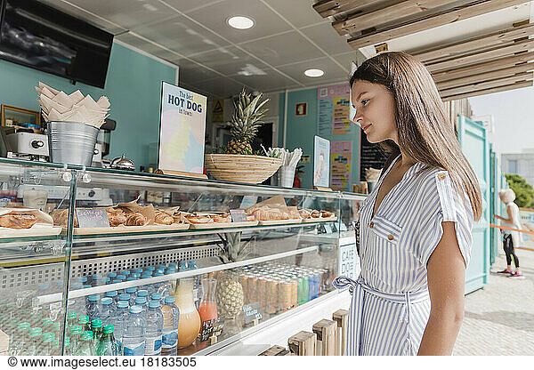 Young woman standing by display at bakery on sunny day