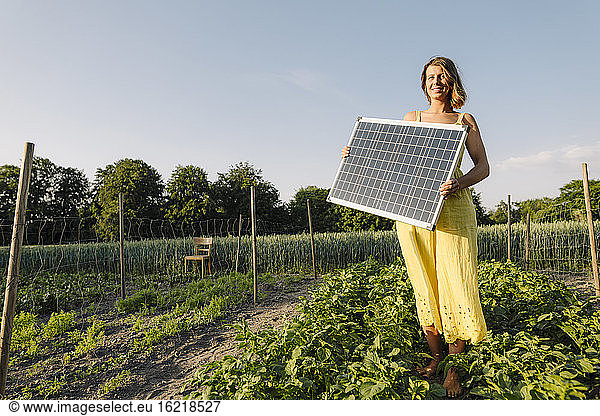 Young woman standing in a vegetable patch in the countryside holding solar panel