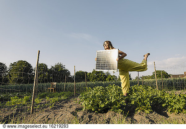 Young woman standing in a vegetable patch in the countryside holding solar panel