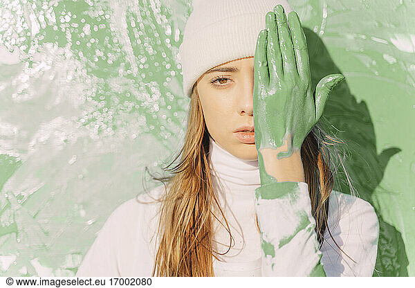 Young woman standing in front of painting  covering eye with green hand