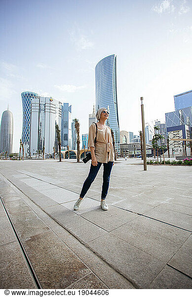 Young woman standing in front of skyscrapers in Doha