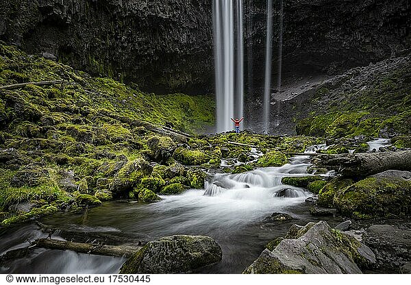 Young woman standing in front of waterfall  stretching her arms in the air  Tamanawas Falls  long time exposure  Cold Spring Creek wild river  Oregon  USA  North America