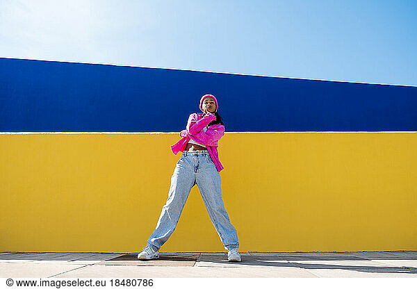 Young woman standing in front of yellow wall on sunny day