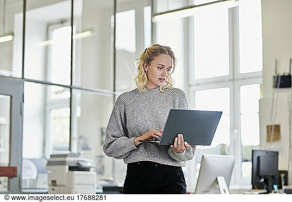 Young woman standing in office using laptop