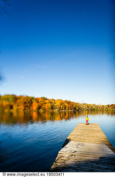 Young woman standing on boat dock next to river with fall colors
