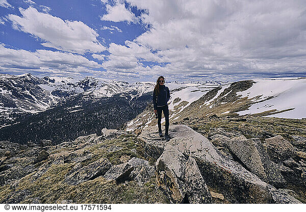 Young Woman standing on exposed rock in a snowfield in Rocky Mountains