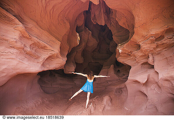 Young woman standing on one leg with arms outstretched in cave