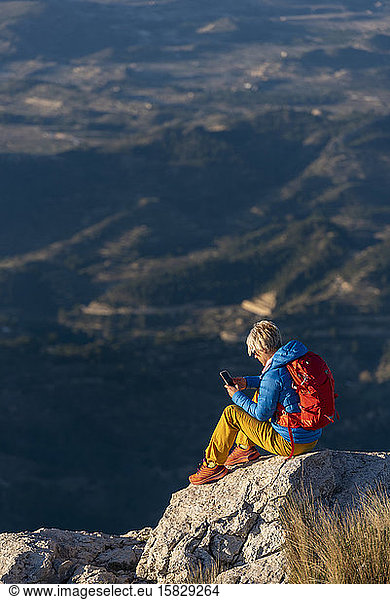 Young woman standing on rocks on top of a mountain with mobile phone.