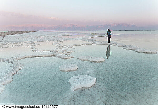 Young woman standing on salt formations in dead sea at sunset