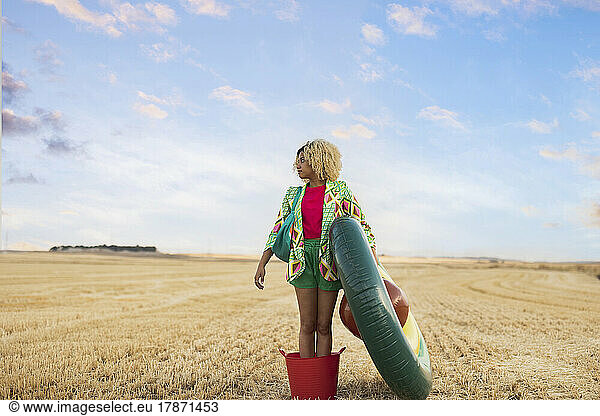 Young woman standing with avocado shaped inflatable ring at field