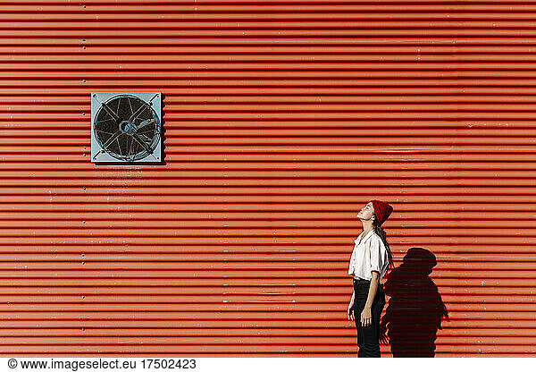 Young woman standing with eyes closed at red corrugated wall