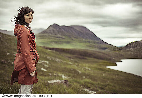 young woman stands on mountain looking at view of loch in scotland