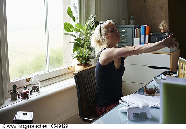 Young woman stretching arms at desk in home office