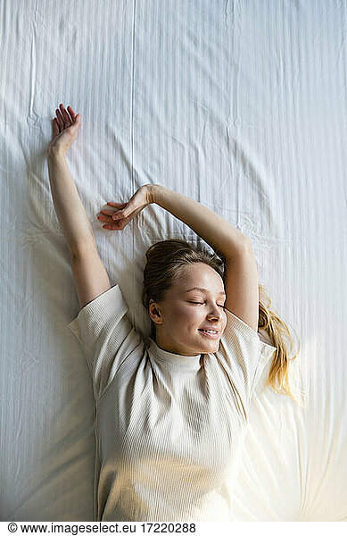 Young woman stretching hand while napping on bed