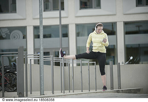 Young woman stretching her leg on railings and listening to music  Bavaria  Germany