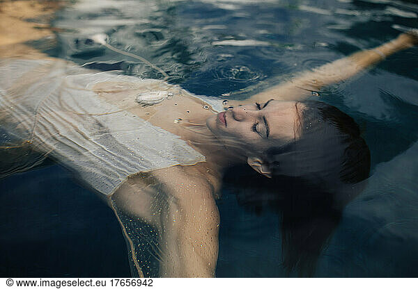 Young woman swimming underwater in white dress