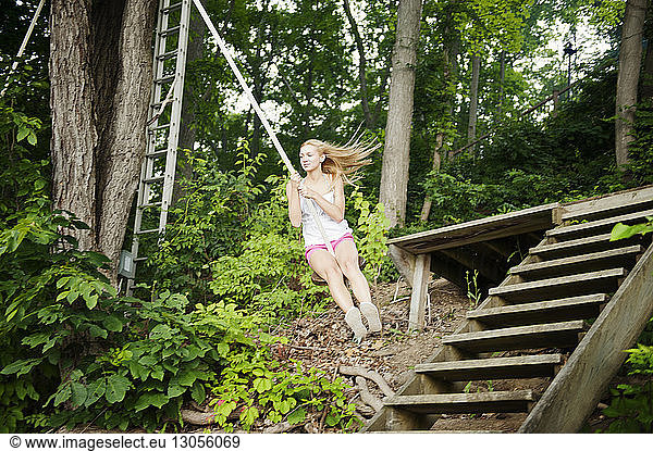 Young woman swinging on rope by staircase in forest