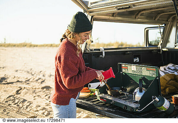 Young woman tailgate cooking while beach car camping alone