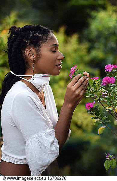 Young woman takes face mask off to smell the flowers