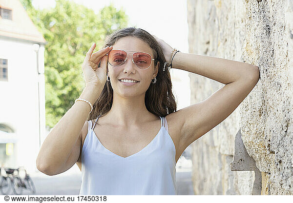Young woman taking hold on sunglasse and smiling at the camera
