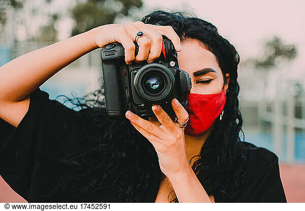 Young woman taking photo with camera wearing face mask