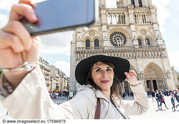 Young woman taking selfie on smart phone with Notre Dame Cathedral