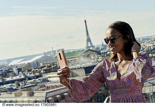 Young woman taking selfie through smart phone with Eiffel Tower in background  Paris  France