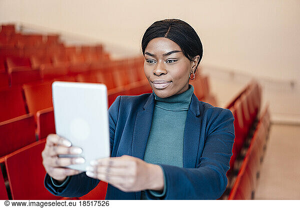 Young woman taking selfie through tablet PC in auditorium