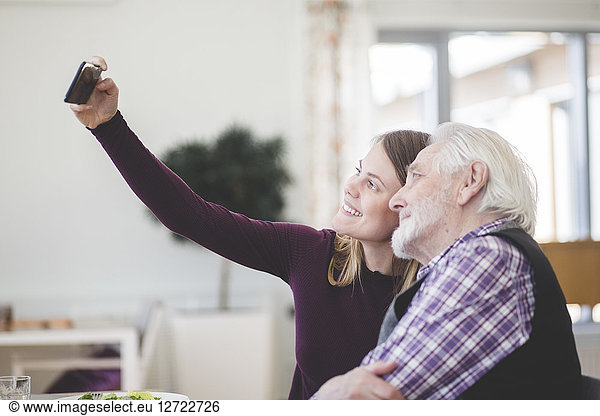 Young woman taking selfie with grandfather while sitting in nursing home