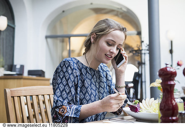Young woman talking on mobile phone while eating salad at restaurant