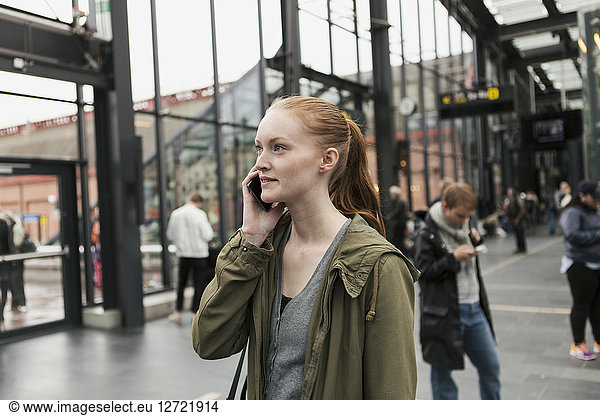Young woman talking on mobile phone with friend in background at city