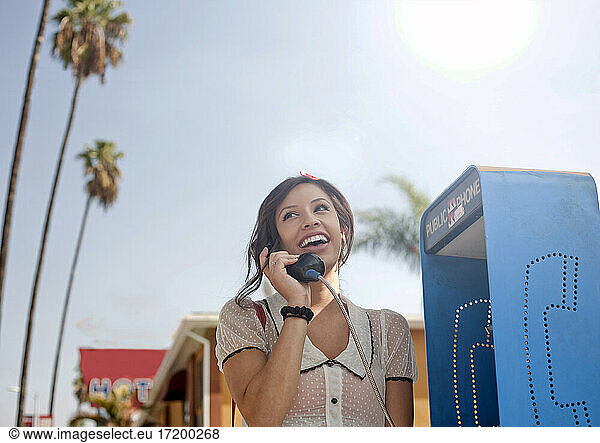 Young woman talking on pay phone while standing against sky