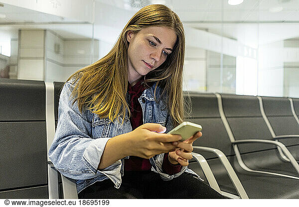 Young woman text messaging through smart phone at airport lobby
