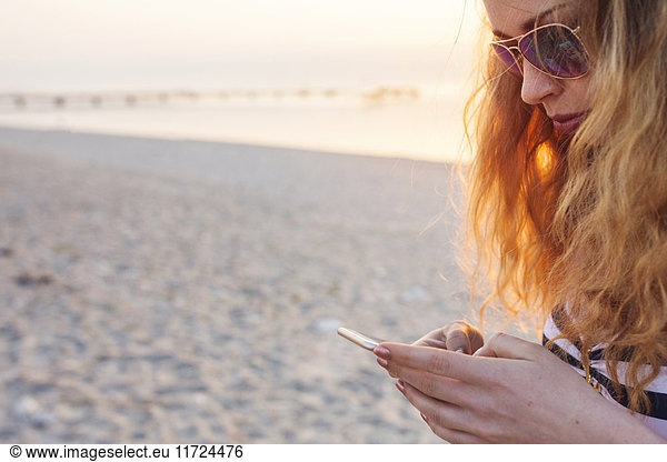 Young woman texting on beach at sunset
