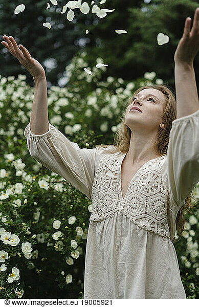 Young woman throwing petals by white flower bush
