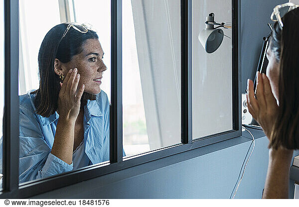Young woman touching face looking in mirror at home