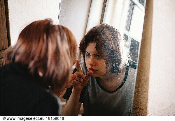 Young woman touching her reflection looking in the mirror at home