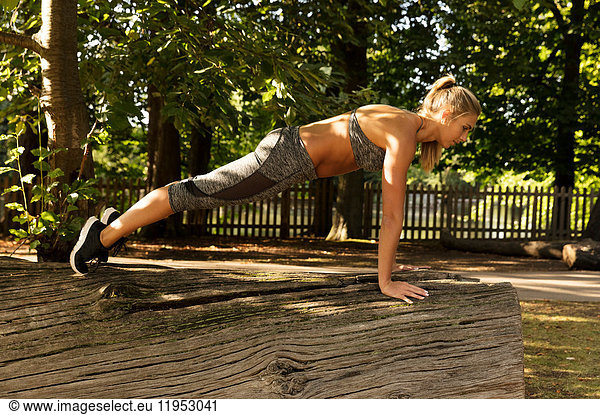 Young woman training in park  doing push ups on log