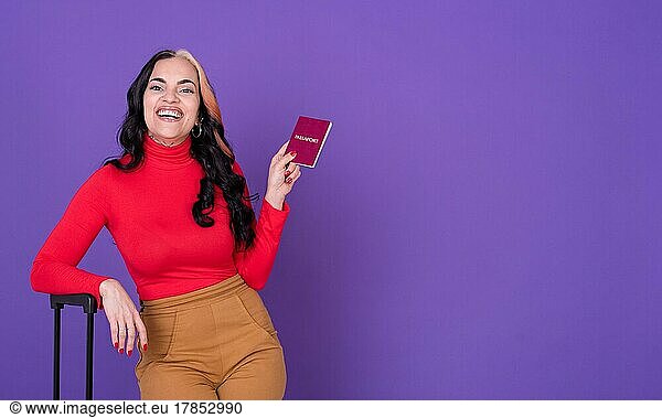 Young woman traveler with passport and suitcase against purple background