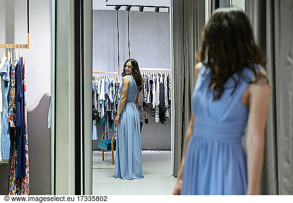 Young woman trying on blue dress while looking in mirror at boutique