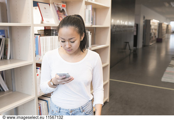 Young woman using cell phone in library