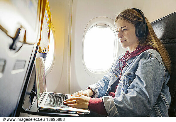 Young woman using laptop and listening music in airplane