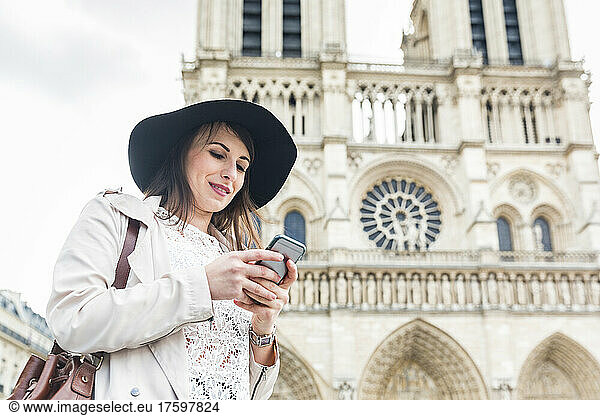 Young woman using mobile phone by Notre Dame Cathedral
