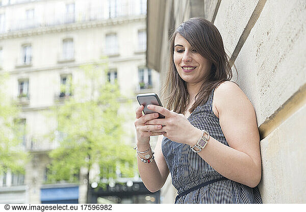 Young woman using mobile phone by wall