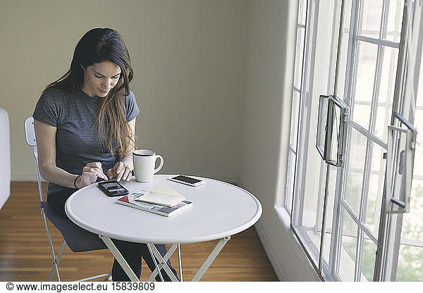 Young woman using mobile phone while having coffee in living room at home