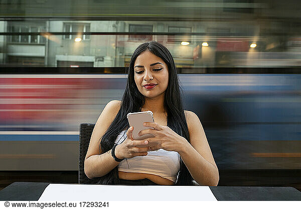 Young woman using mobile phone while sitting at table in cafe during dusk