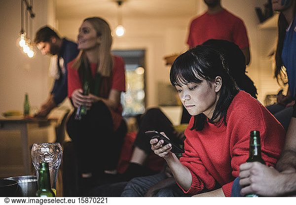 Young woman using mobile phone while sitting with friends at home