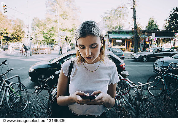 Young woman using mobile phone while standing on sidewalk in city