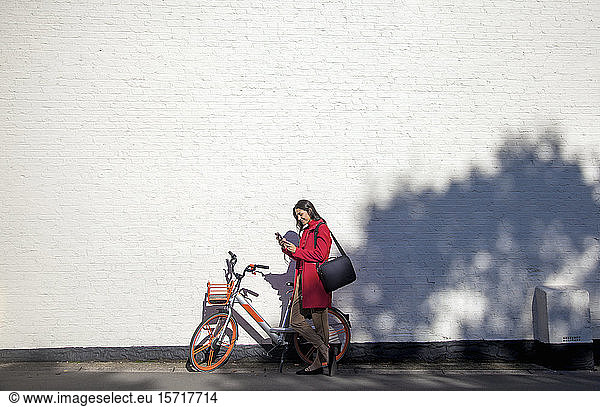 Young woman using rental bike with smartphone app l